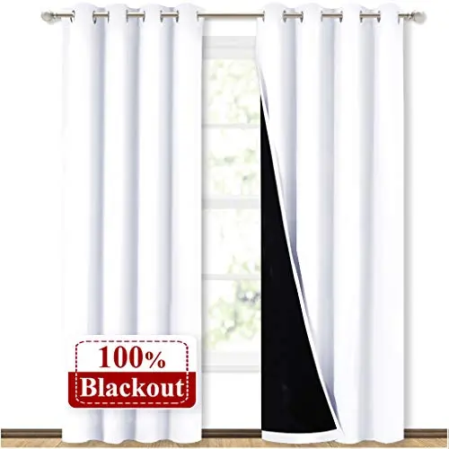 NICETOWN pure white blackout curtain panels with grommets, hanging to block light.