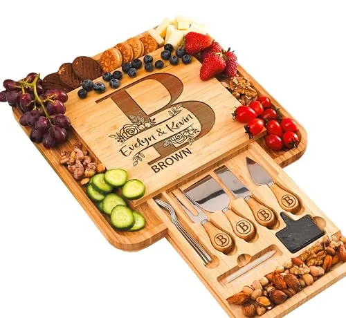 A large, square bamboo charcuterie board with a personalized laser engraving, featuring a hidden drawer stocked with cheese knives and serving utensils.