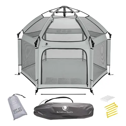 POP 'N GO baby playpen unfolded on a sandy beach, showing its large mesh walls and sun canopy.